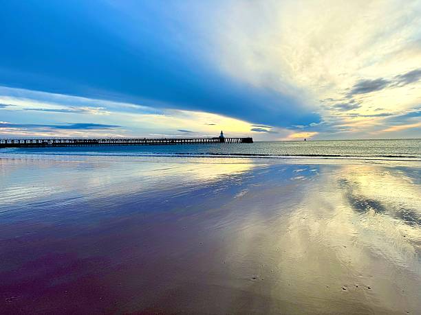 istock Dramatic cloudscape reflecting on wet sand with a pier and lighthouse at Blyth in Northumberland 2243181360