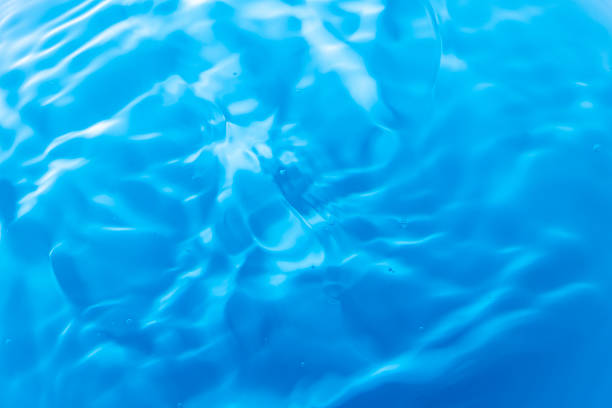 Blue water with ripples on the surface. Defocus blurred transparent blue colored clear calm water surface texture with splashes and bubbles. Water waves with shining pattern texture background.