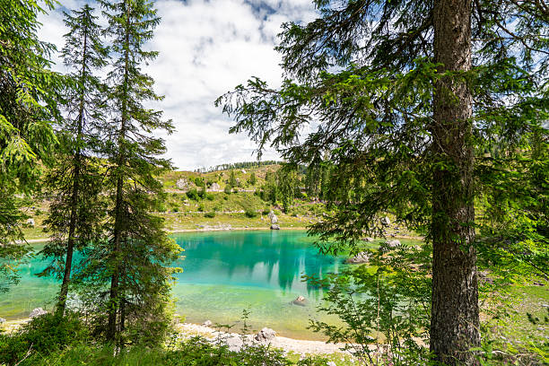 Scenic view of the famous Lago di Carezza (Karersee) in the Dolomites, northern Italy. The emerald lake is surrounded by dense pine forest and overlooked by the impressive Latemar mountain range. A peaceful alpine landscape capturing the beauty of nature, reflection, and the harmony between water, forest, and rock — perfect for concepts of wilderness, travel, and eco-tourism.
