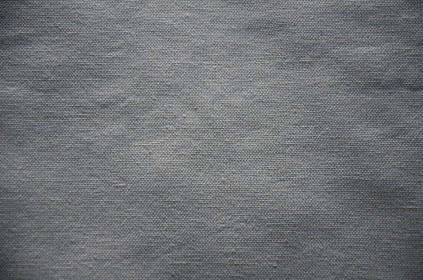 Detailed macro shot of a coarsely woven gray fabric, likely natural linen or heavy cotton canvas. The background features a rough, basket-weave pattern in muted charcoal or slate gray, ideal for rustic, industrial, or textile design concepts.