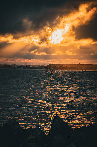 istock Dark Ocean Waves Beneath a Fiery, Dramatic Sunset Sky Over an Industrial Horizon. 2243191545