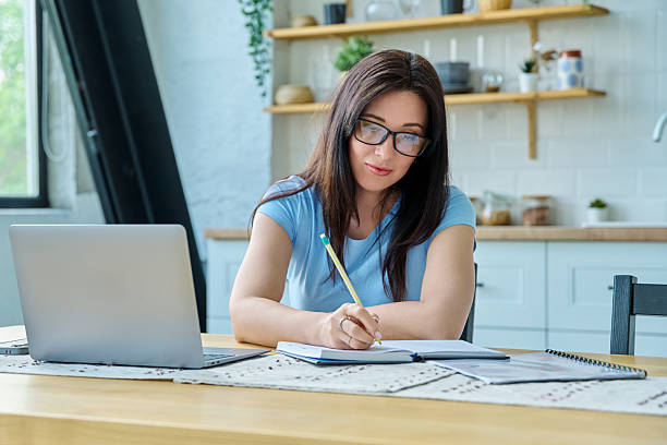 istock Young serious woman working with laptop sitting at table at home 2243203099