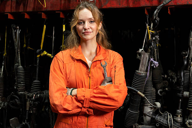 Mid adult English female auto mechanic working in home garage on a vintage 4x4 vehicle. She is dressed in work clothes. Interior of private garage of private home in Spring, Texas.