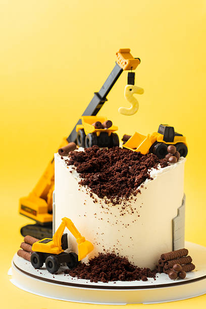 istock Birthday cake for five year old kid, decorated with construction vehicles. Heavy car themed homemade cake for toddler boy birthday celebration with toy excavators and crane on the yellow background. 2243208402