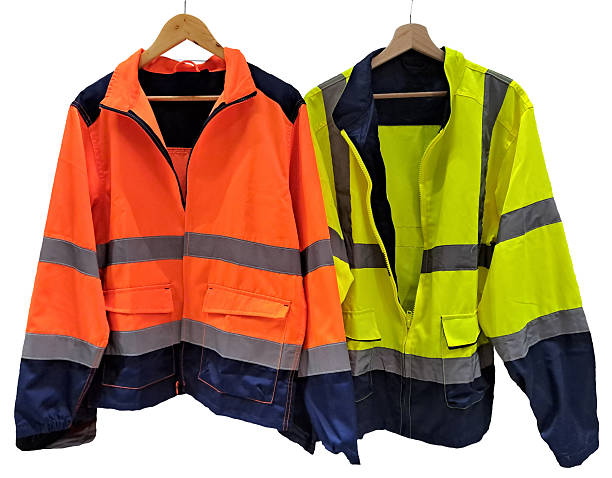 istock HIGH VISIBILITY SAFETY JACKETS ON HANGERS - Fluorescent orange and yellow reflective workwear clothing for industrial, construction and road workers, protective uniform for visibility and safety 2243215836