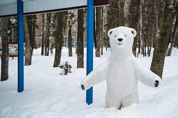 In a serene winter park, a charming stuffed polar bear stands motionless in the pristine snow, creating a picturesque scene that captures the essence of the seasons frozen beauty