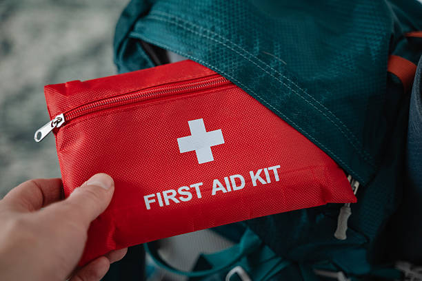 istock An individual is standing and holding a first aid kit right in front of a large backpack, which is usually used for carrying personal items on journeys or outdoor activities 2243217319