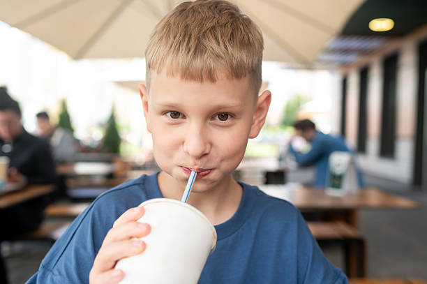 Casual moment of a boy relaxing at an open-air cafe in summer, holding a cold drink and enjoying the warmth, freshness, and carefree atmosphere of the day