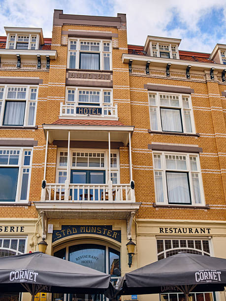 Winterswijk, Netherlands – October 16, 2025: Historic hotel-restaurant Stad Munster with yellow-brick facade, ornate balcony and Cornet-branded umbrellas on the town square.