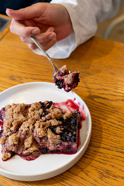 Cranberry crumble, crisp in a baking dish. Woman eating forest fruit crumble with a fork.