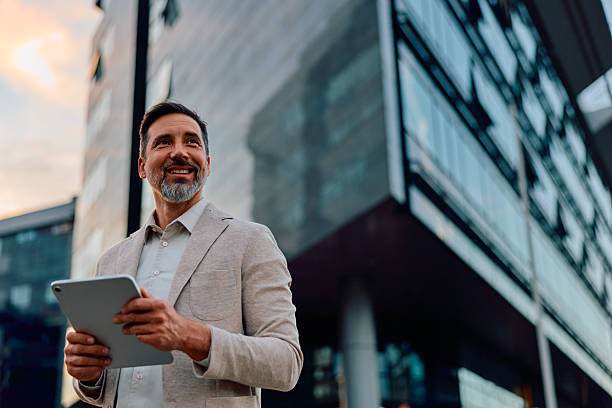 istock Happy businessman holding tablet looking away in urban setting 2243236990