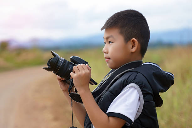 istock Young boy holding and looking through a professional camera outdoors. Photography hobby, learning, and future career concept. 2243240648