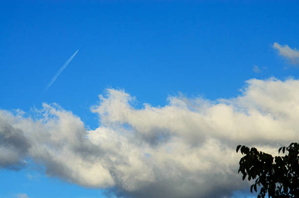 The bright blue sky is filled with puffy white clouds and a jet stream, creating a stunning visual display