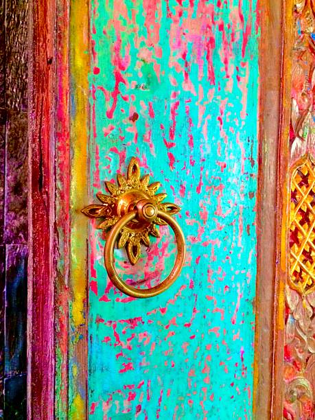 A vibrantly weathered wooden door in Ubud, Bali, featuring a stunning mix of turquoise, pink, and golden hues. The ornate brass door knocker adds a ceremonial elegance, set against a backdrop of tropical decay and sacred artistry. This colorful composition captures the essence of Balinese spirit: timeless beauty, vibrant culture, and mystical serenity. Perfect for travel lovers, bohemian souls, or design inspirations rooted in sacred places.