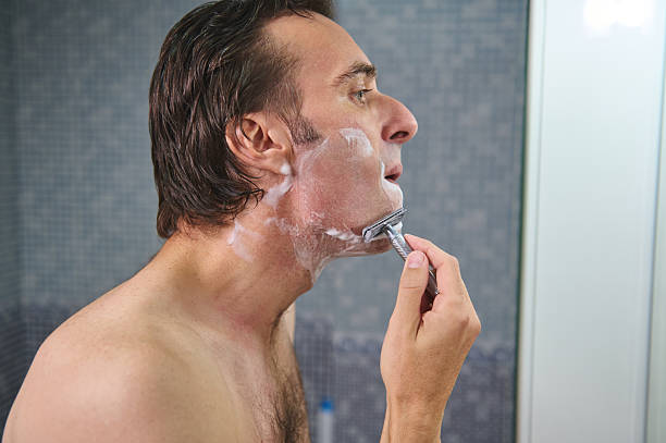 Man Shaving With Razor and Foamy Lather in Bathroom Mirror Reflection