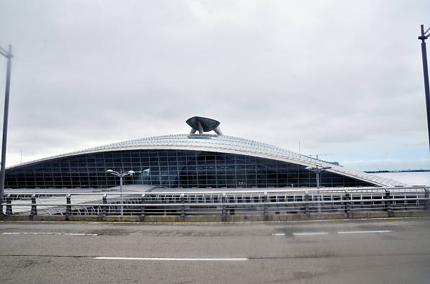 A sleek terminal structure rises beside the waterfront at Incheon International Airport in South Korea, its curved roof and circular skylight evoking themes of aerodynamic design and global transit. Framed by roadways and glass panels, the building anchors a gateway of movement, modernity, and civic spectacle. Seoul, South Korea. August 23, 2013