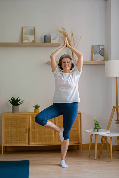 istock Senior woman practicing yoga tree pose at home, focusing on balance 2243288040