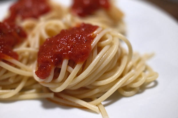 Stock photo shows a mouthwatering image, tongs are used to lift spaghetti from a cooking pan, covered in rich ragu sauce, fresh tomatoes, and garnished with fragrant basil leaves. This scene perfectly represents traditional Italian cuisine,