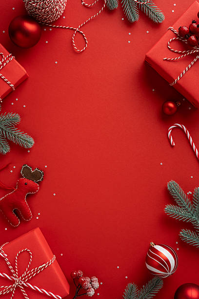 istock Vertical scene features red gifts, ornaments, pine branches and candy canes arranged for Christmas and New Year greeting on a bold red backdrop 2243294800