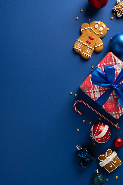 istock A vertical festive holiday scene featuring a wrapped gift box, a gingerbread cookie, ornaments and candy canes on a blue backdrop 2243294876