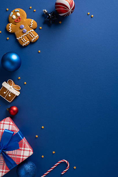 istock Bright vertical holiday scene with a gingerbread man, presents, ornaments, candy cane, and ribbons on a blue backdrop perfect for Christmas and New Year greetings and festive mood 2243294885