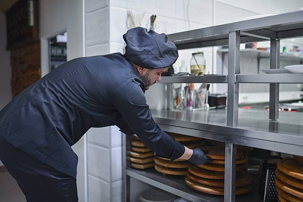 istock Professional Chef Organizes Wooden Pizza Peel Stack Under Stainless Steel Kitchen Shelves In Busy Restaurant 2243295879
