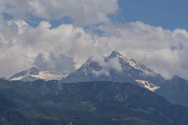 Snow capped mountain peaks above forest slopes and clouds