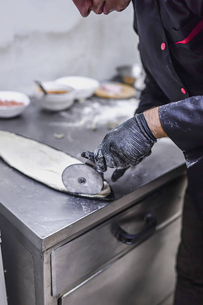 istock Professional Chef Rolling Dough With Pizza Cutter In A Stainless Steel Kitchen Studio 2243300952