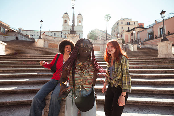 Three young women of diverse ethnic backgrounds spending joyful moments together at the famous Spanish Steps in Rome, Italy.