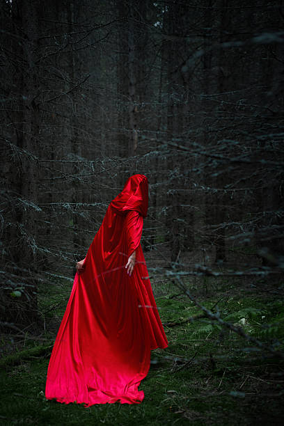 istock mysterious woman dressed in a vibrant red cloak wanders through a dark, dense forest at dusk. atmosphere is eerie yet enchanting, surrounded by tall trees 2243317582