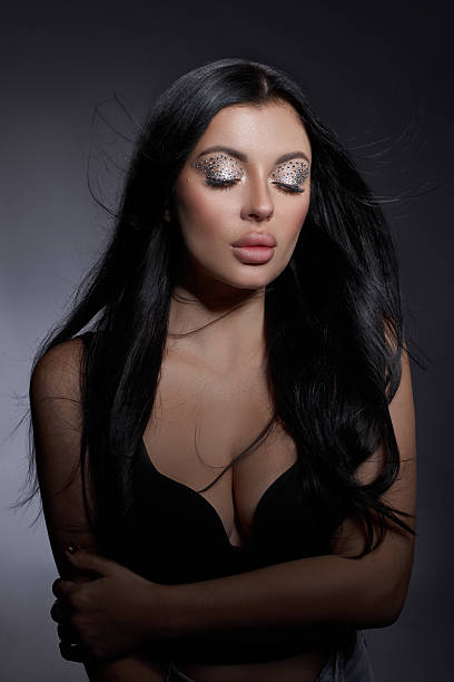 istock model stands confidently with her eyes closed, showcasing bold makeup and shiny embellishments on her eyelids. Her long hair flows softly around her shoulders, enhancing the artistic vibe 2243317593