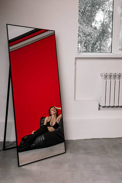 istock model sits gracefully on a black bean bag in a modern room. Reflections in a large mirror highlight the vivid red wall and the stylish setting. atmosphere is artistic and contemporary 2243317628