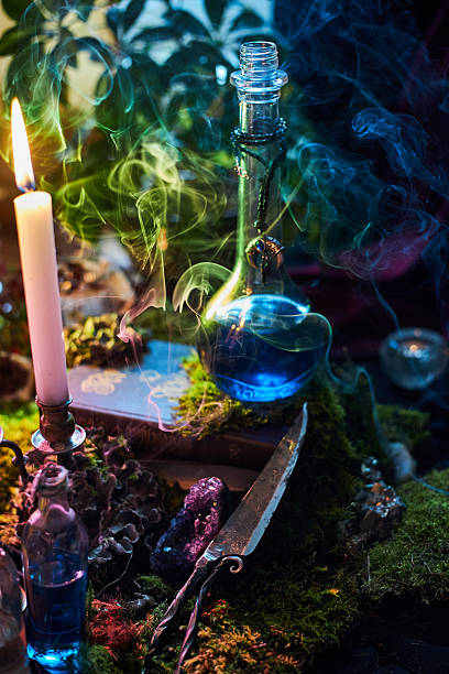 istock glass bottle filled with a vibrant blue potion sits on a wooden surface surrounded by moss, candles, and swirls of colorful smoke. atmosphere feels magical and enchanting 2243317646