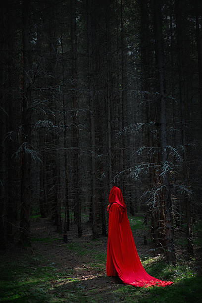 istock figure dressed in a striking red cloak stands amidst tall, dark trees in a shadowy forest. scene captures a sense of mystery and enchantment during twilight 2243317651