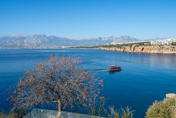 A tour boat sails peacefully along the dramatic cliffs of Antalya, surrounded by the deep blue waters of the Mediterranean