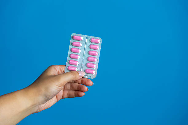 istock Hand Holding Blister Packs of Pink Pills on Blue Background 2243328708