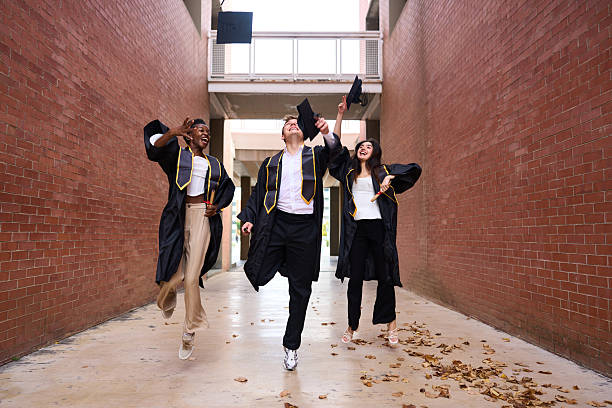 Group of students in graduation gowns throwing their mortarboards in the air on the university campus outdoors.
