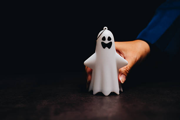 istock Cute Halloween Ghost Candle with Black Face and Bow Tie Held by a Hand in a Dark Environment 2243338293
