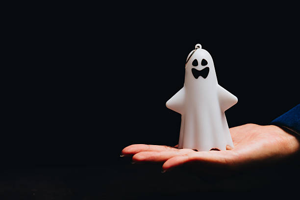 istock Playful white ghost figure in hand with smiling face on dark background for Halloween decoration and spooky themes 2243338298