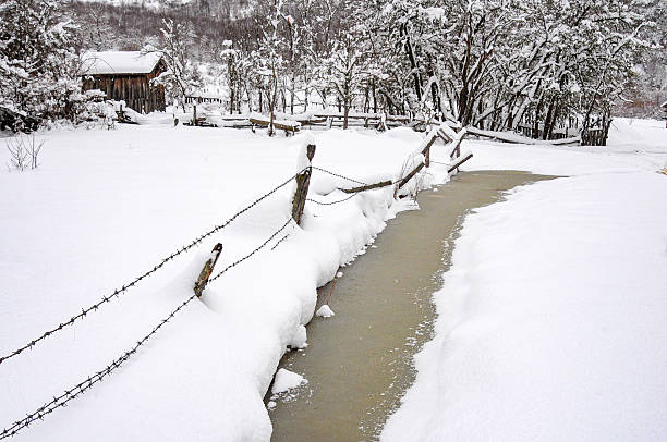 A distant log house and wire fence in winter