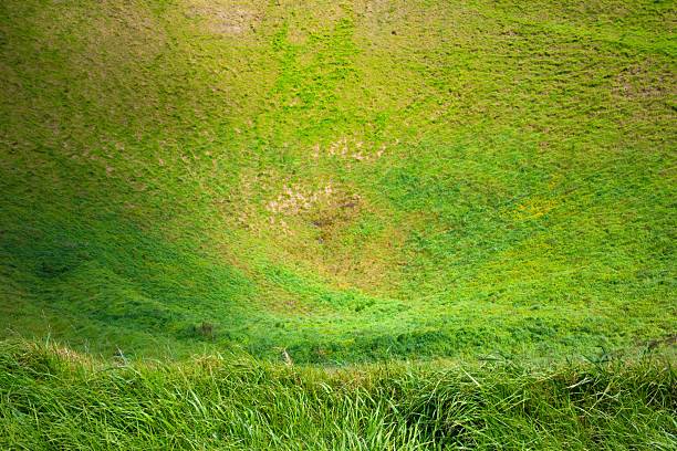 Gentle wind is blowing through crater of an extinct volcano covered with green grass under blue sky in summer time.