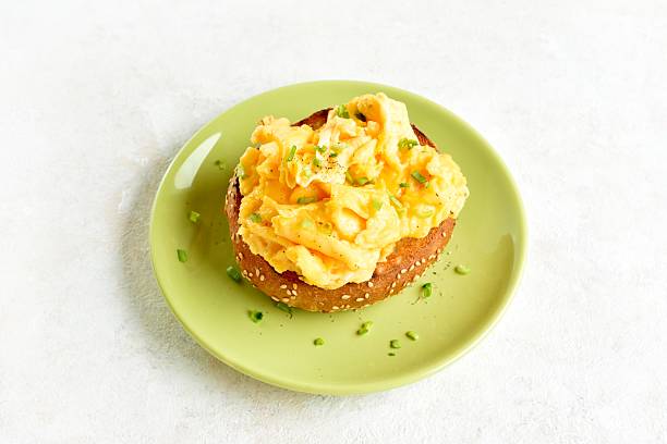 Diet scrambled eggs on toasted brioche bun on green plate on light background. Tasty meal for breakfast or brunch. Close up view