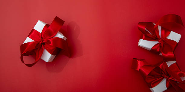 White gift boxes with red ribbons on red background. Festive backdrop for banner, advertising or holiday greeting design.