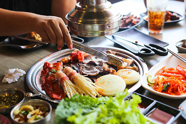 istock Korea BBQ style restaurant. Asian traditional pickle vegetable ingredients on table with people grilling background. 2243364539