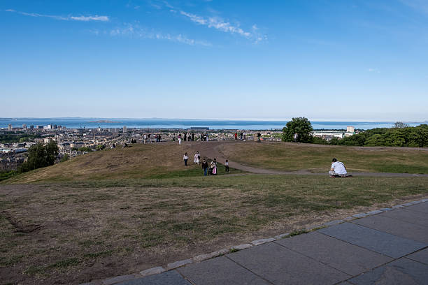 Panoramic view from Arthurs Seat in Edinburgh, Scotland, showcasing the cityscape, rolling green hills, and overcast skies