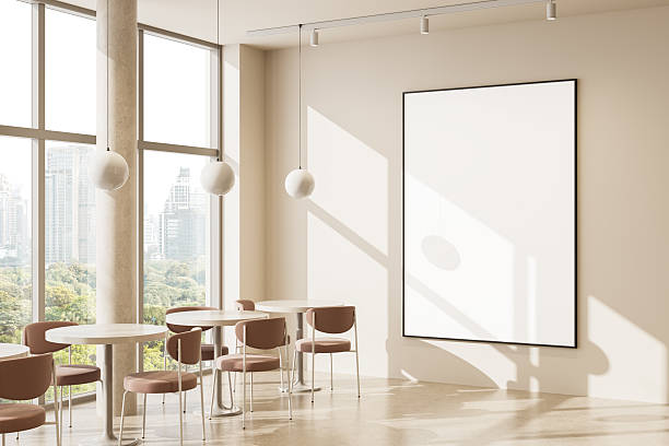 Modern cafe interior with blank poster frame on beige wall and large windows overlooking city skyline in soft daylight ambiance. 3D Rendering