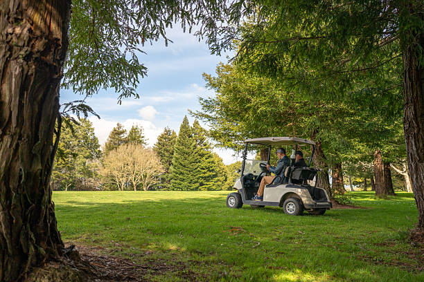 A group of golfers ride in a golf cart on a picturesque golf course, surrounded by the vibrant colors of autumn. Majestic trees with golden leaves create a serene and peaceful atmosphere. This image captures a moment of leisure and enjoyment in the great outdoors, perfect for golf enthusiasts.