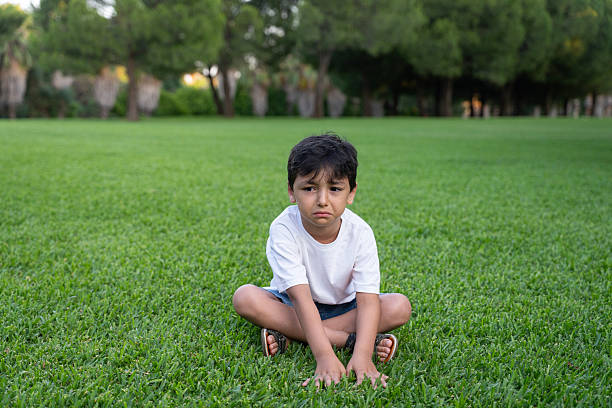 istock Upset Little Boy Sitting on Grass in Park 2243374198
