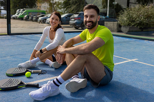 A fit, happy couple sits casually on the padel court, smiling at the camera. This image represents the modern, active lifestyle associated with the sport, perfect for promoting wellness, recreation, and community engagement.