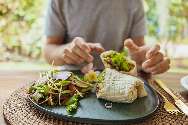 Man about to eat a fresh wrap sandwich with leafy greens and vegetables on a blue plate. Casual meal with healthy salad and nutritious lunch options. Person enjoying balanced food.